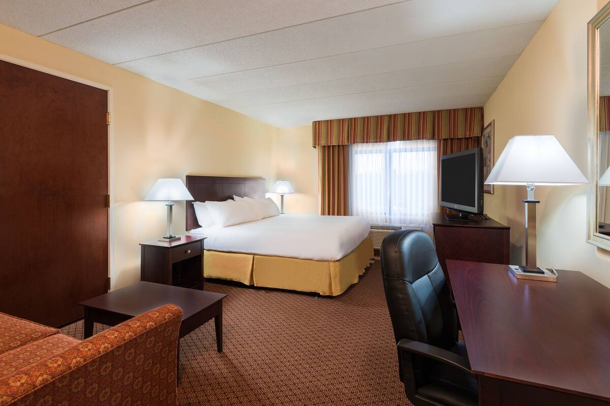 A hotel room with a bed, two bedside tables with lamps, a desk, a chair, and a television.