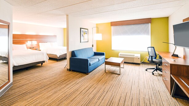 A hotel room with two beds, a blue sofa, a desk with a chair, a TV, and a window with blinds. - Holiday Inn Express Richmond Airport by IHG (Sandston)