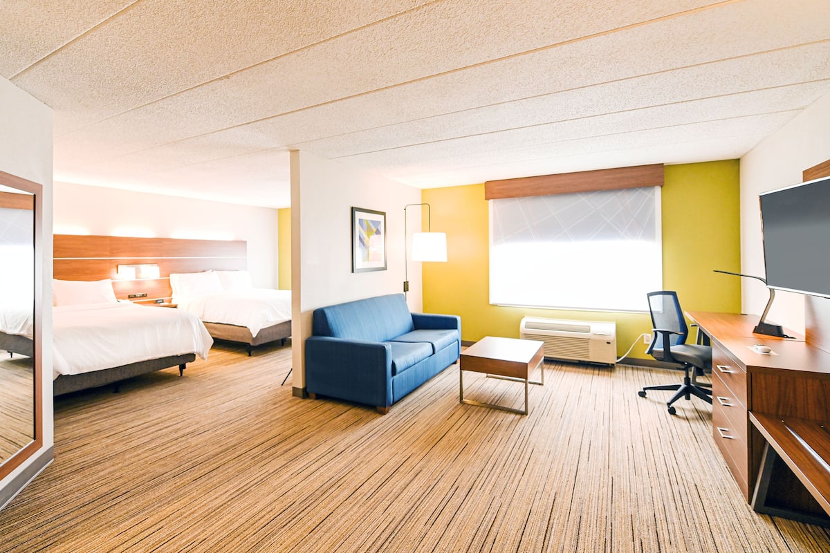 A hotel room with two beds, a blue sofa, a desk, a chair, and a TV.