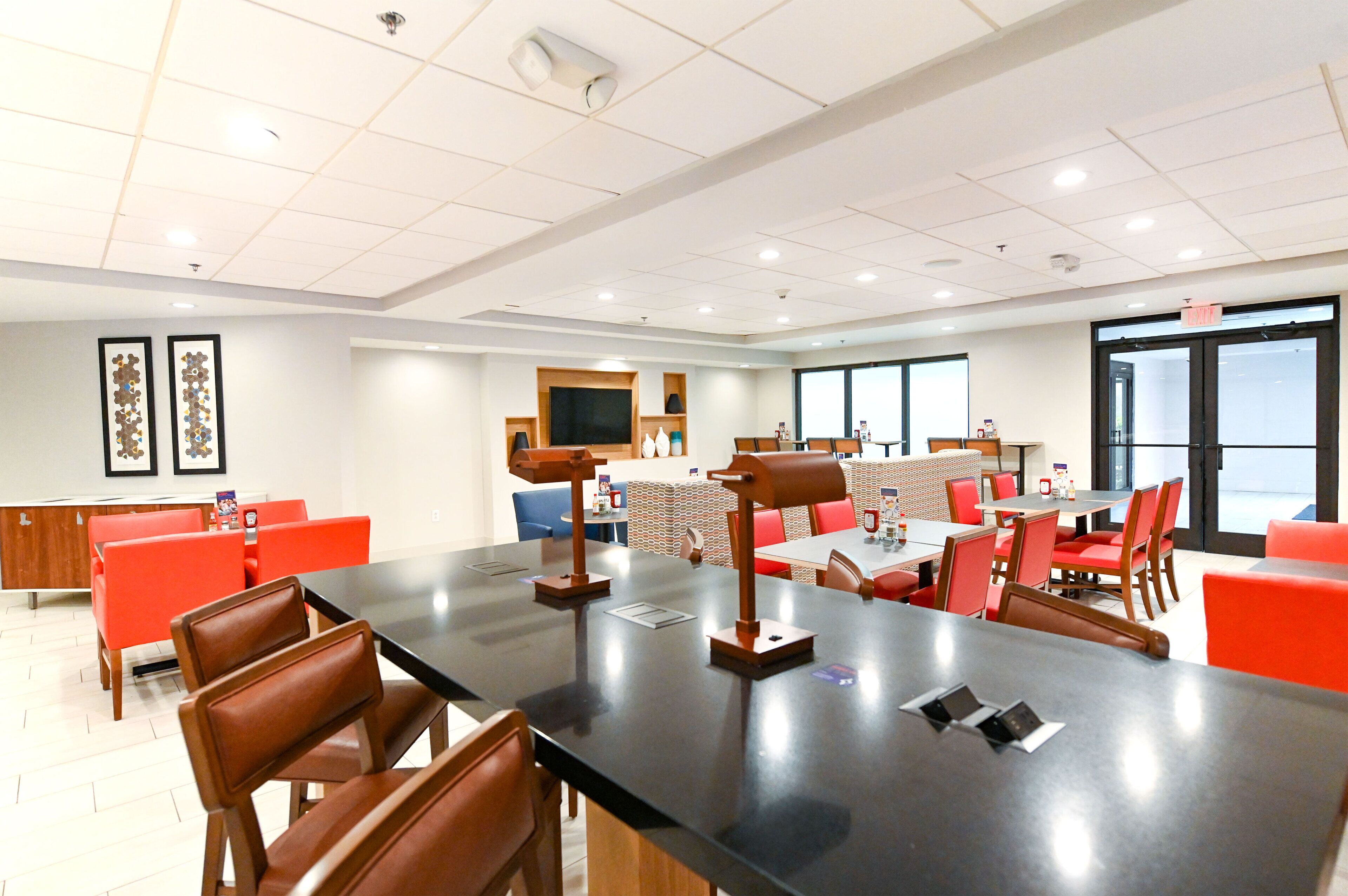 A conference room with a long table, red chairs, and a television.