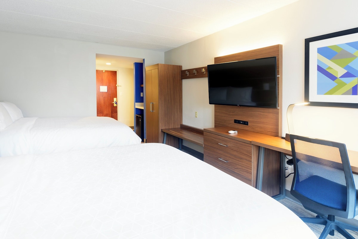 Quarto de hotel com duas camas, uma escrivaninha, televisão de tela plana, uma cadeira e um armário.