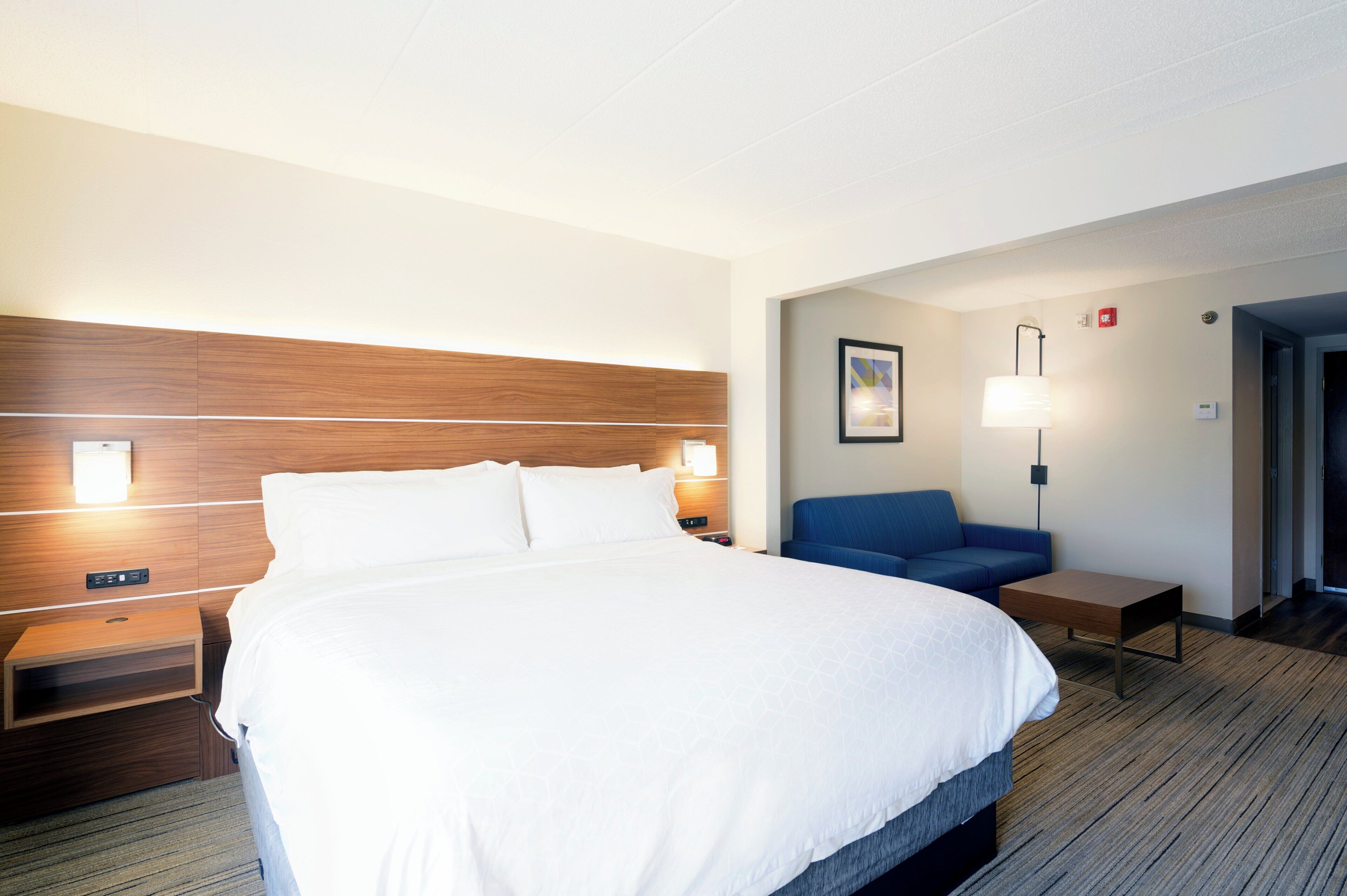 Une chambre d’hôtel avec un grand lit, des tables de chevet, un bureau, une chaise et une lampe fixée au mur.