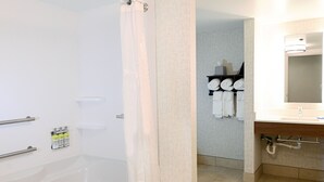A modern bathroom with a bathtub, a shower curtain, a towel rack with towels, a sink with a mirror, and a towel dispenser. - Holiday Inn Express Richmond Airport by IHG (Sandston)