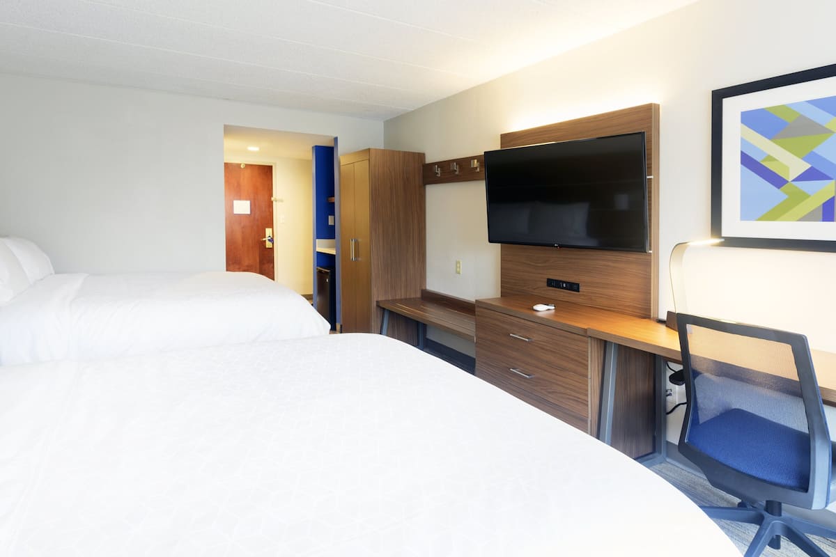 A hotel room with two beds, a desk with a computer, a TV, and a framed picture on the wall.