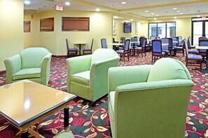 A hotel lobby with green upholstered chairs, a wooden table, and patterned carpet. - Holiday Inn Express Richmond Airport by IHG (Sandston)