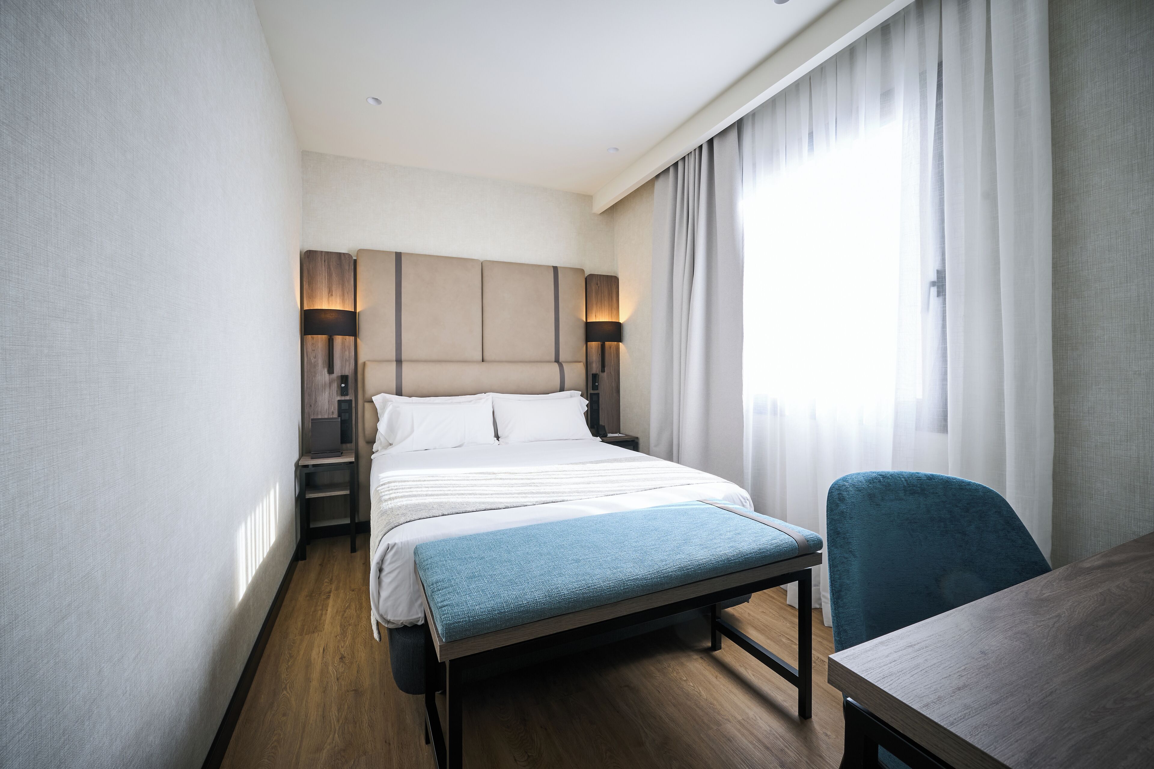 A modern hotel room with a large bed, bedside tables, a desk, and a chair.