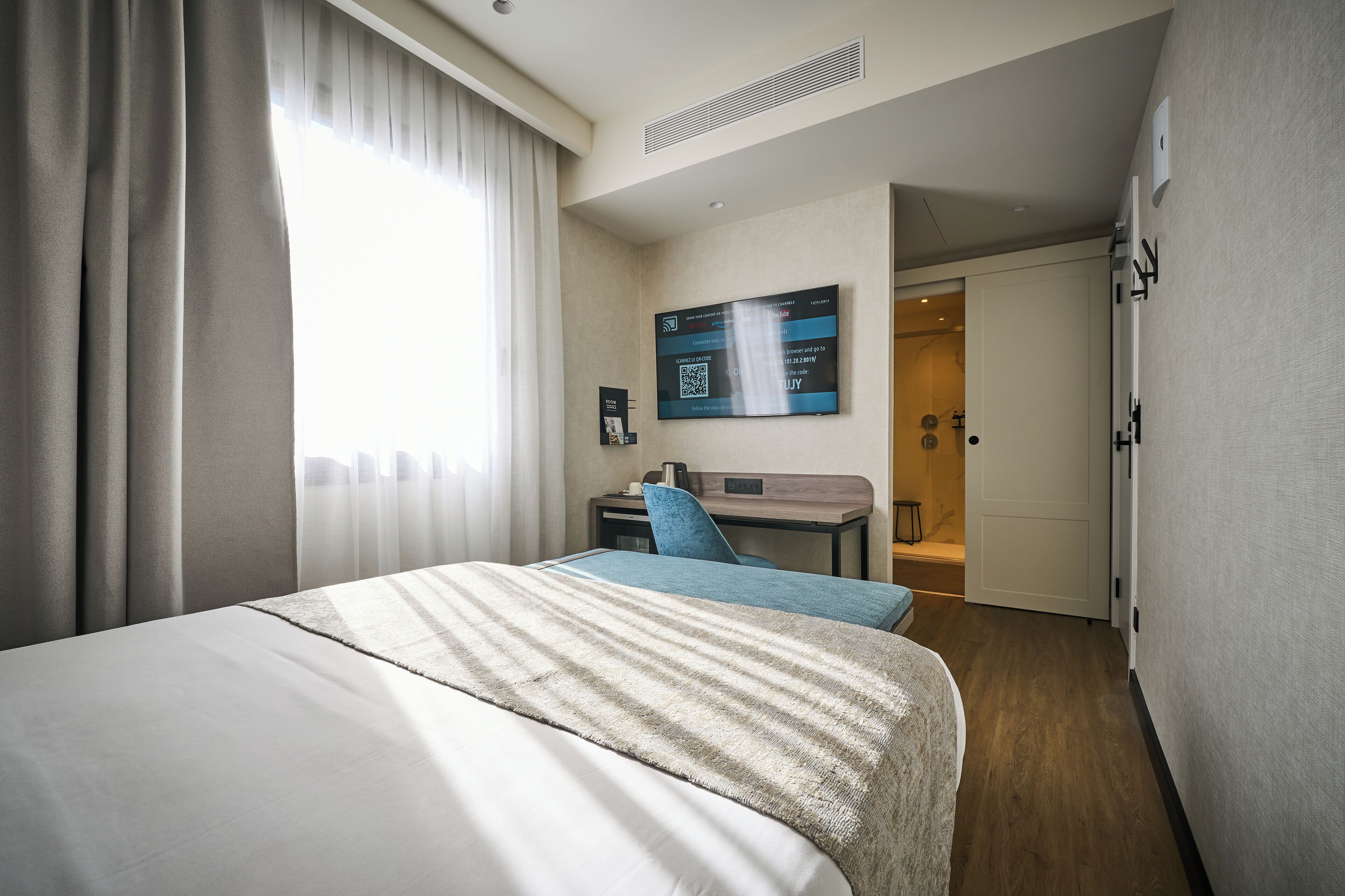 A hotel room with a large bed, a desk, and a TV mounted on the wall.