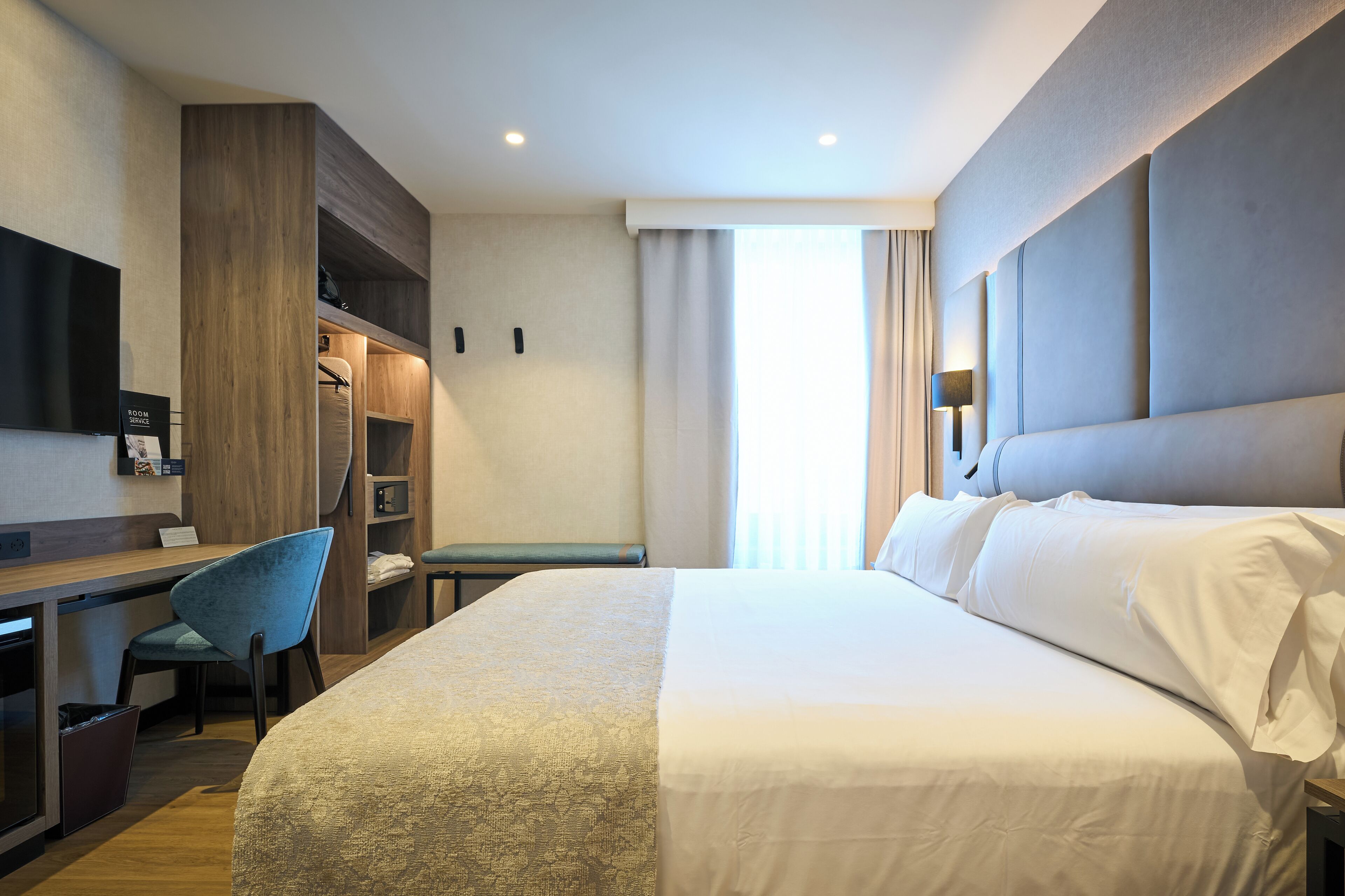 Quarto de hotel com uma cama grande, uma escrivaninha com cadeira, televisão e guarda-roupa.