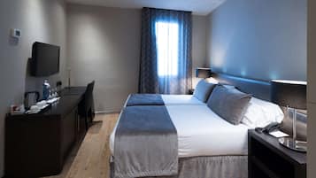 Una habitación de hotel moderna con una cama grande, un escritorio, un televisor de pantalla plana y un ventanal con cortinas.