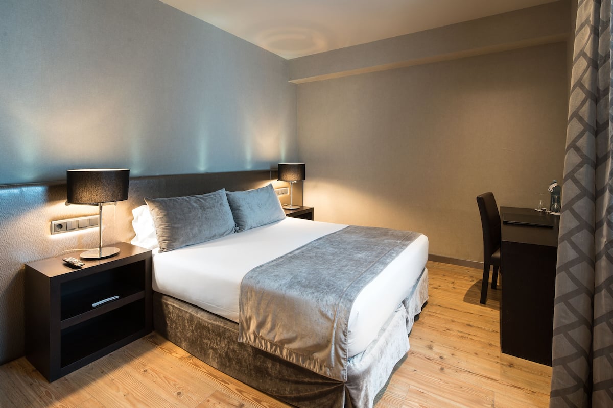A neatly made bed with a grey blanket, two bedside lamps, and a small nightstand with a remote control.