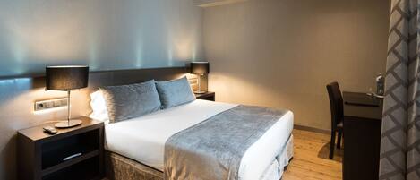 A neatly made bed with a grey blanket, two bedside lamps, and a small nightstand with a remote control.