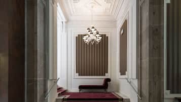 Eine prächtige Treppe mit rotem Teppich und einer Bank, die zu einem Raum mit einem großen Fenster und einer Kristallleuchtre zu führen scheint.