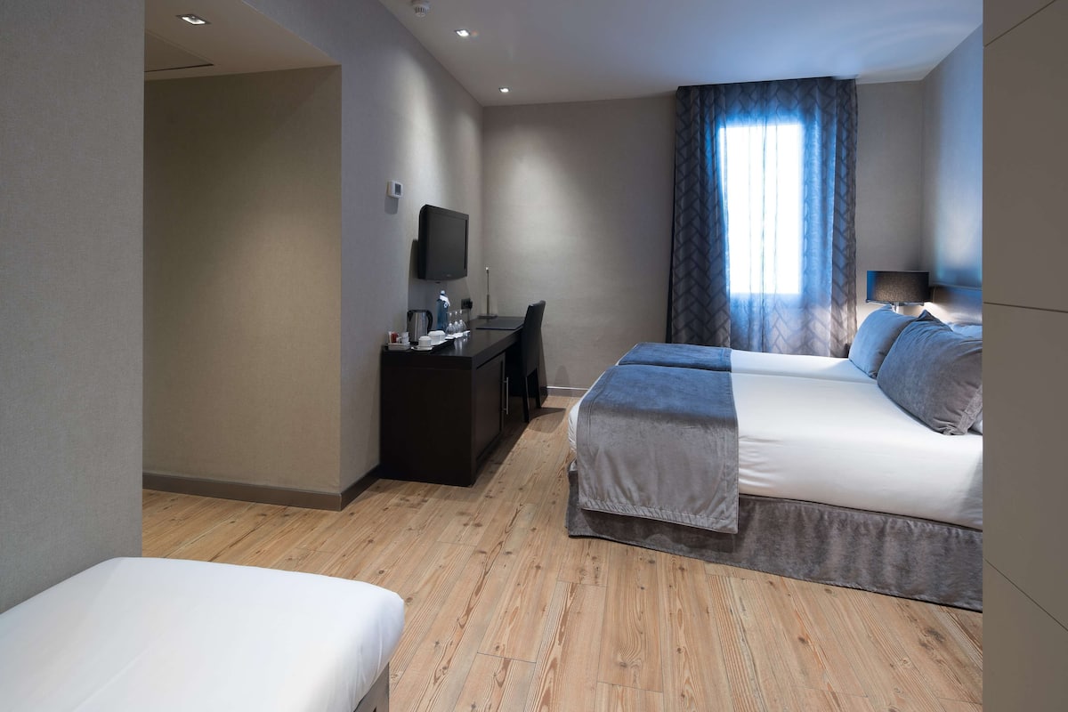 A hotel room with a bed, a desk, a chair, a television, and a window with curtains.