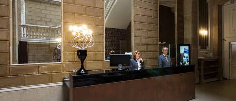 A reception desk with a modern design, a large mirror, and a decorative light fixture.