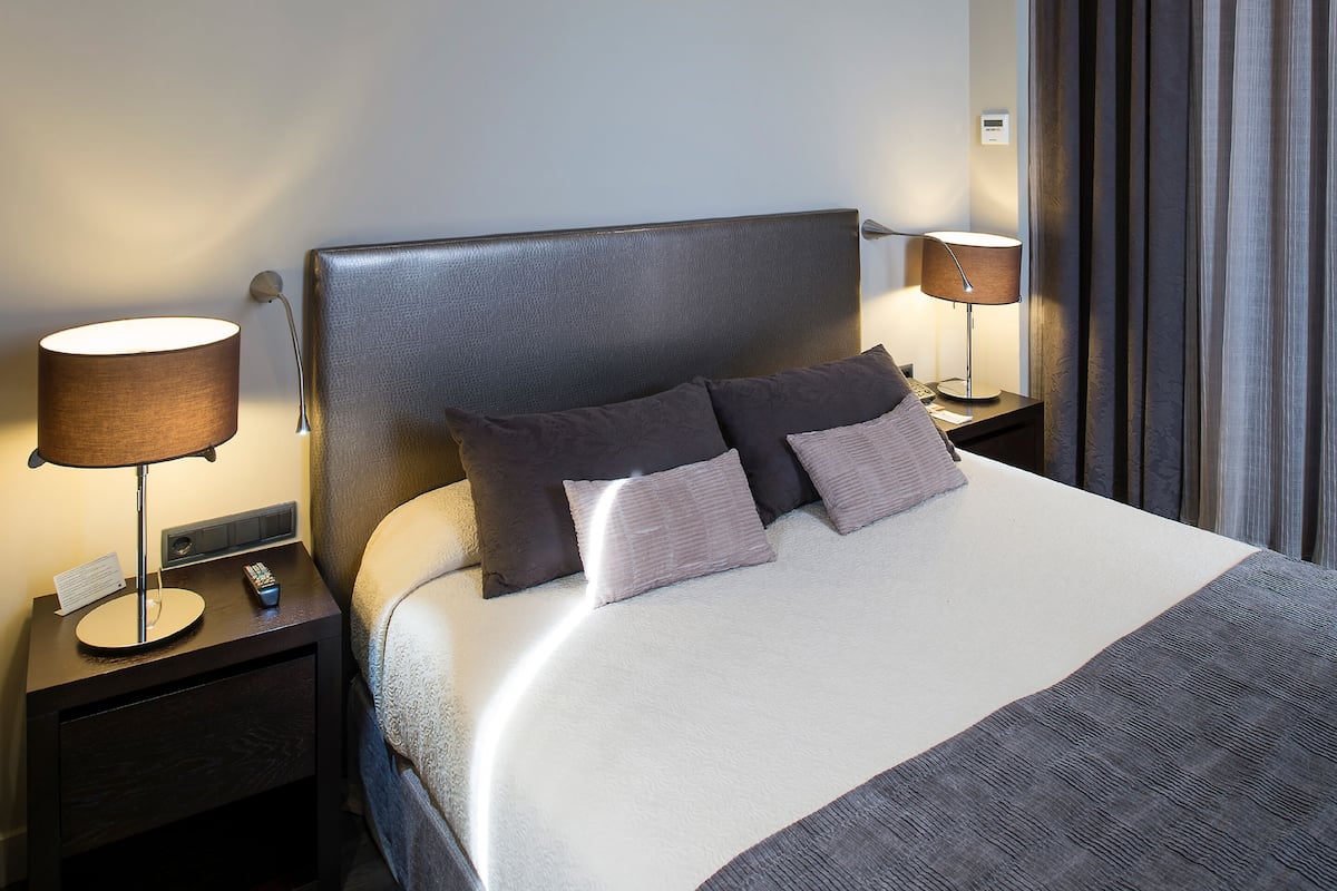 A neatly made bed with a headboard, two bedside tables with lamps, and a remote control on one of the tables.