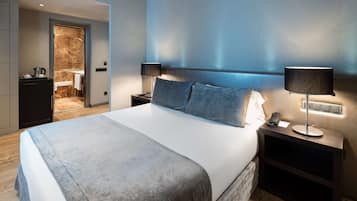 Une chambre d’hôtel moderne avec un grand lit, deux tables de chevet et une salle de bain visible à travers une porte ouverte.