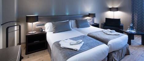 A modern hotel room with two beds, a desk, and a chair.