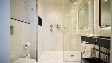 Un baño moderno con ducha envuelta en vidrio, inodoro y tocador con perchero.
