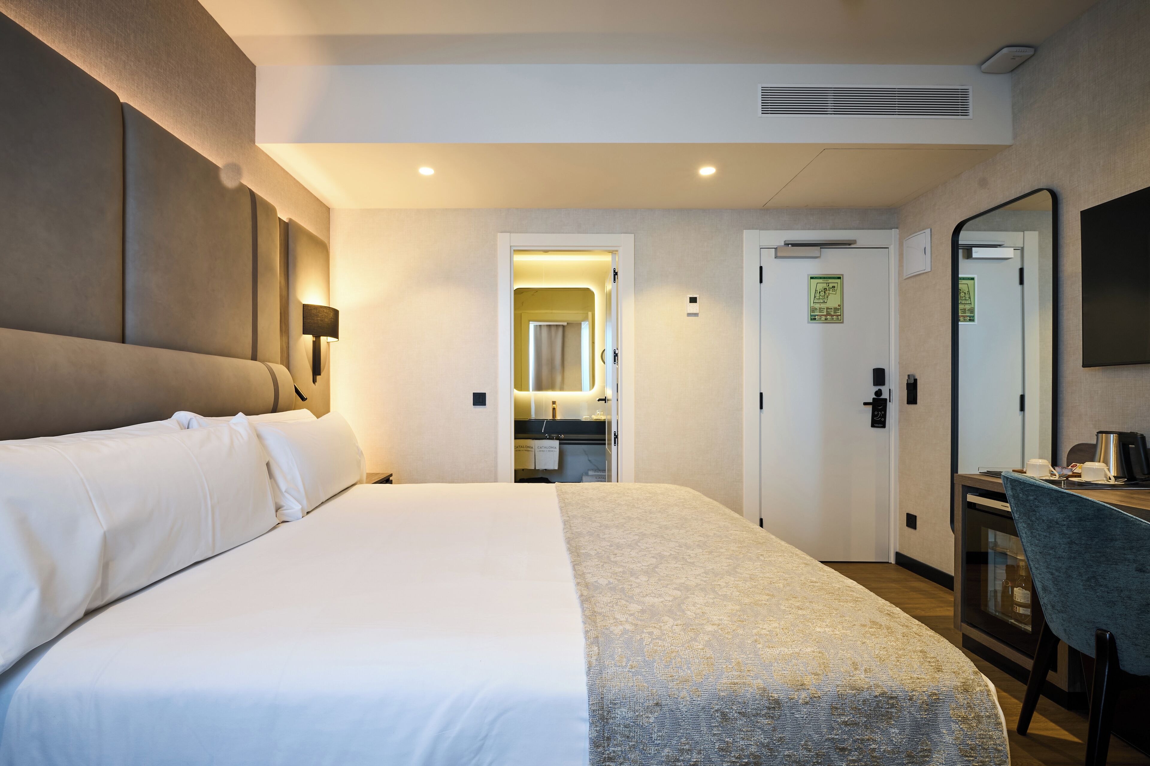 Een hotelkamer met een groot bed, een bureau met stoel, een spiegel en een kitchenette.