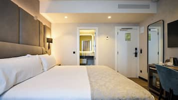 Een hotelkamer met een groot bed, een bureau met stoel, een spiegel en een kitchenette.
