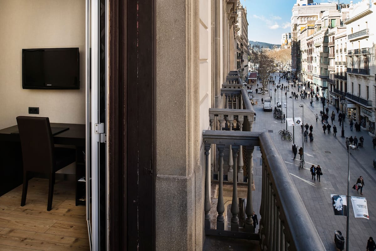 A balcony with a view of a busy street, a flat-screen TV mounted on the wall, and a dining area with a table and chairs.