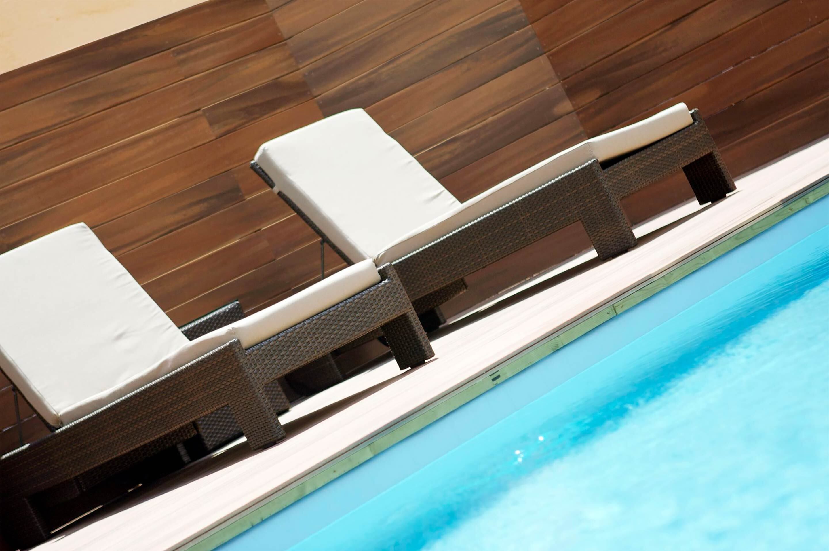 Un espacio de descanso junto a la piscina con sillones de mimbre y cojines blancos.