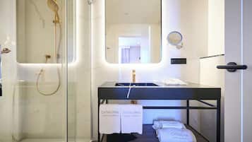 Un bagno moderno con cabina doccia in vetro, un mobile lavabo nero con specchio e uno scaffale con asciugamani recanti la scritta "Catalonia Hotels & Resorts".
