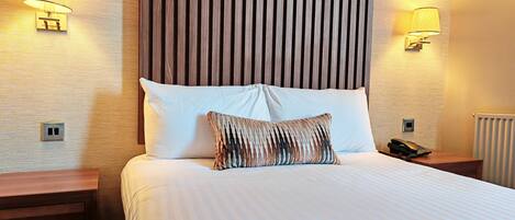 Une chambre d’hôtel avec un grand lit, deux lampes de chevet, une tête de lit en bois et un téléphone sur la table de chevet.