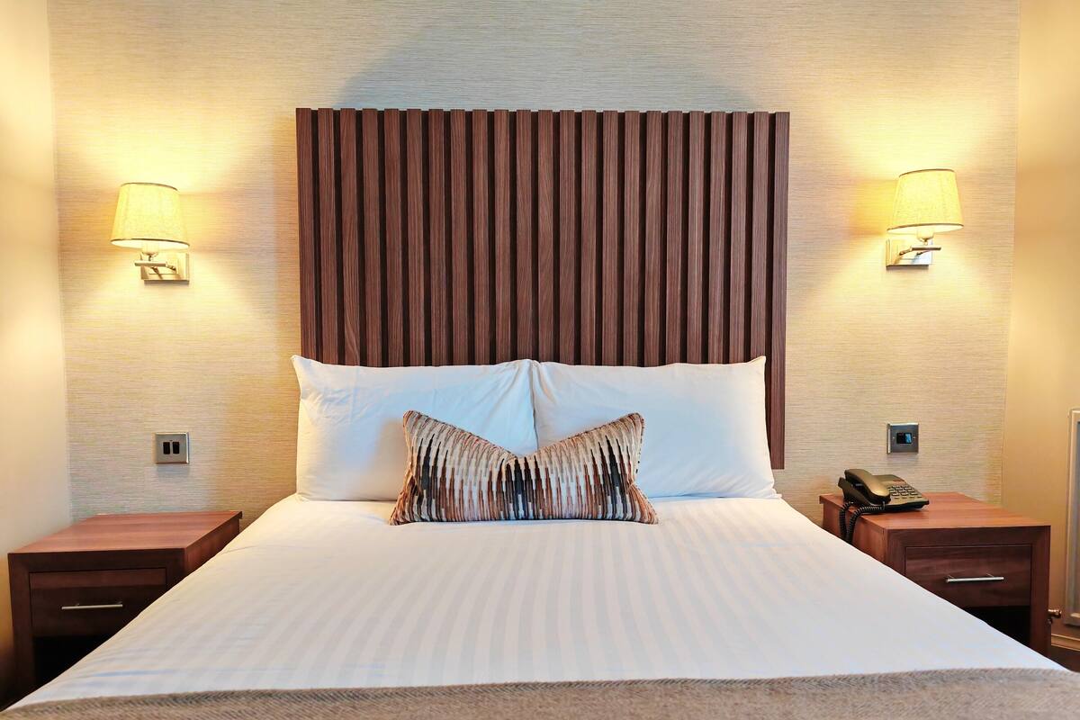 Una habitación de hotel con una cama grande, dos mesitas de noche, un teléfono y lámparas de pared.