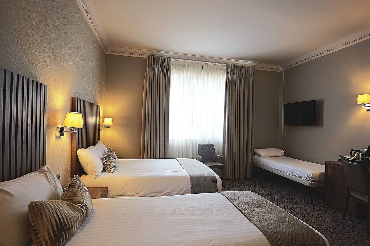 Habitación de hotel con dos camas, un escritorio, una silla, un televisor y una ventana con cortinas.