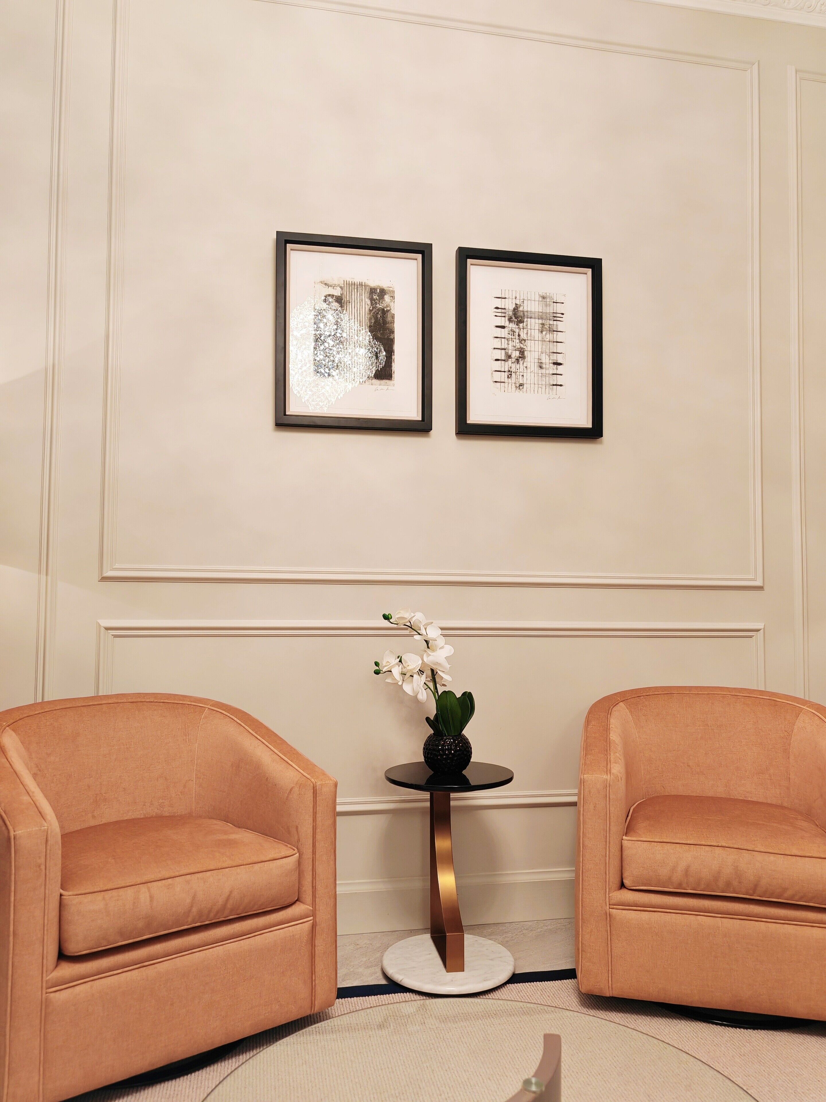 Ein Zimmer mit zwei Ledersesseln, einem kleinen runden Tisch mit einer Vase weißer Blumen und zwei gerahmten Kunstwerken an der Wand.