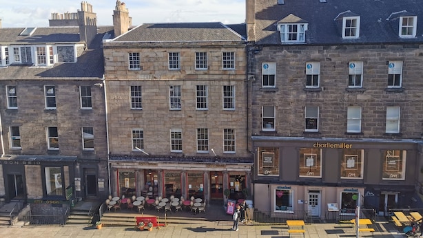 Une vue de rue montrant une rangée d’immeubles avec des cafés et des boutiques.