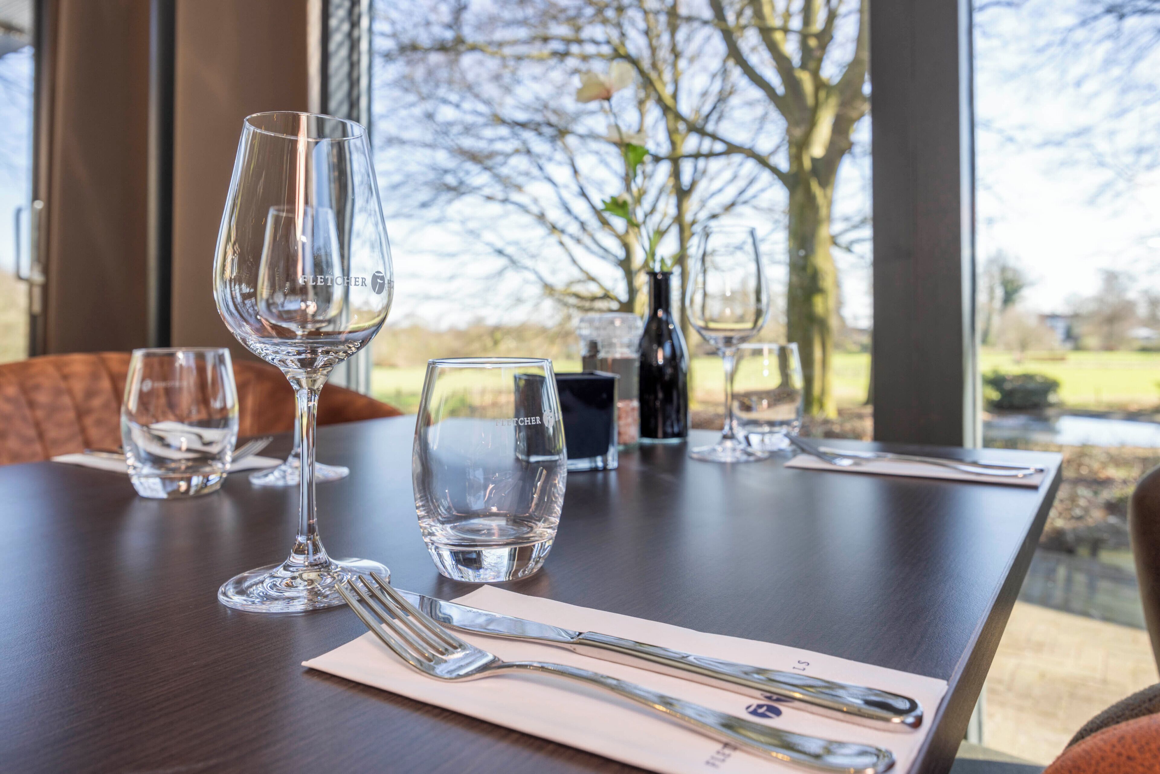 A dining table with empty wine glasses, a bottle, and cutlery.