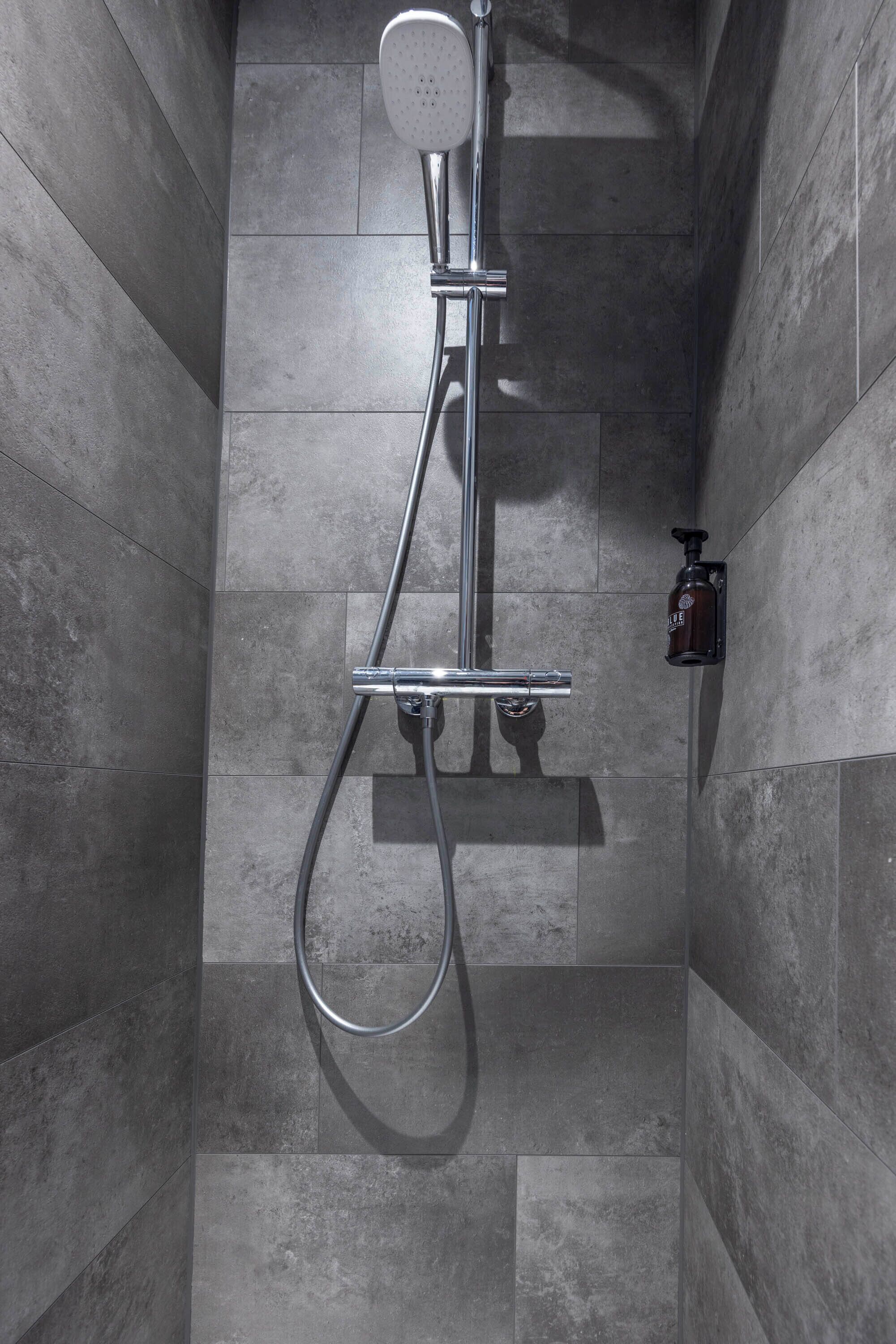 A shower with a handheld showerhead, a wall-mounted faucet, and a soap dispenser.