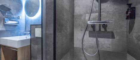 Un baño moderno con ducha de vidrio, lavamanos blanco y espejo con luz circular.