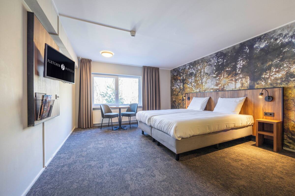 Une chambre d’hôtel avec un lit, un bureau, une chaise, une télévision et une grande fenêtre.
