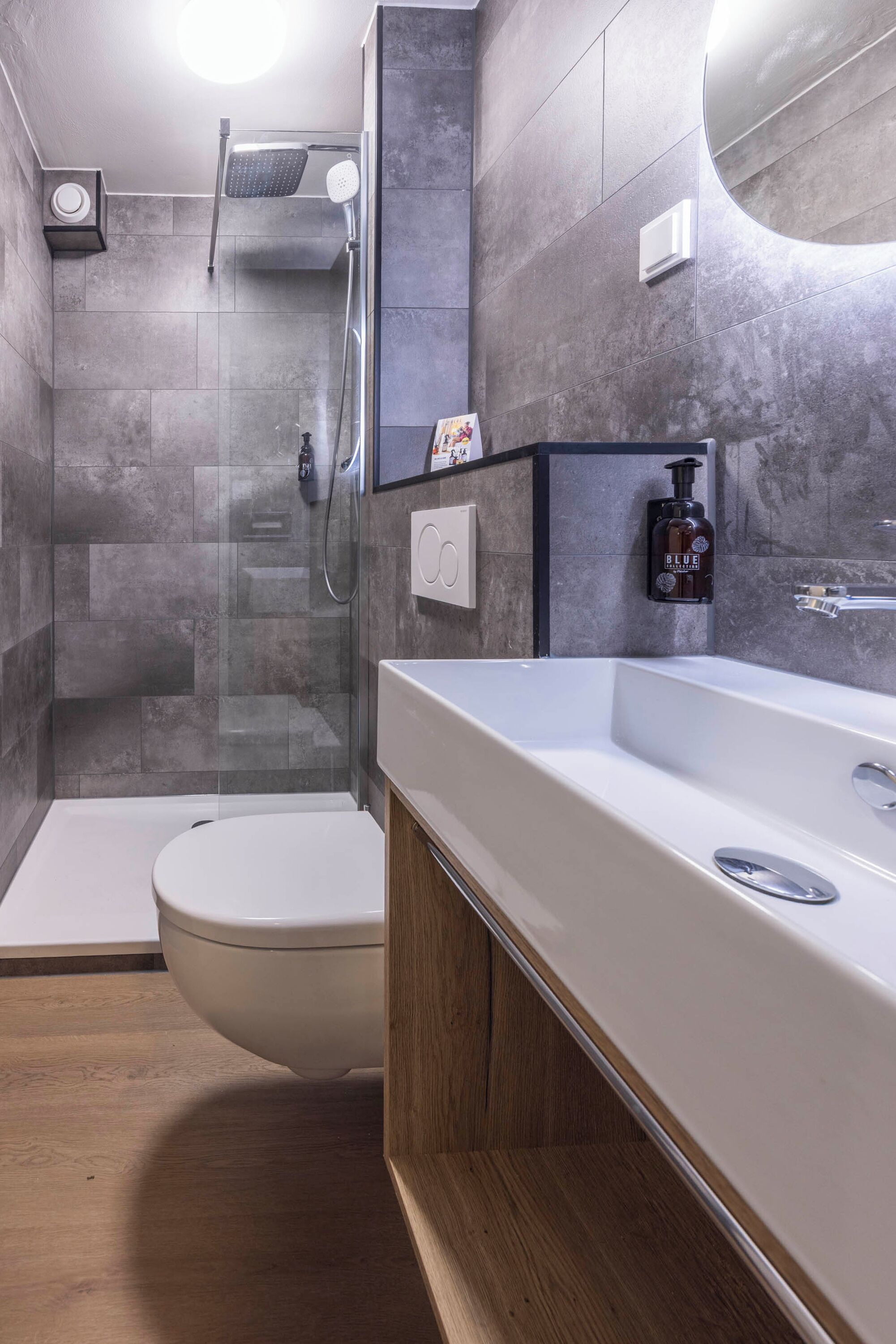 Une salle de bain moderne avec une douche à parois de verre, des toilettes blanches et un meuble-lavabo en bois avec un miroir.