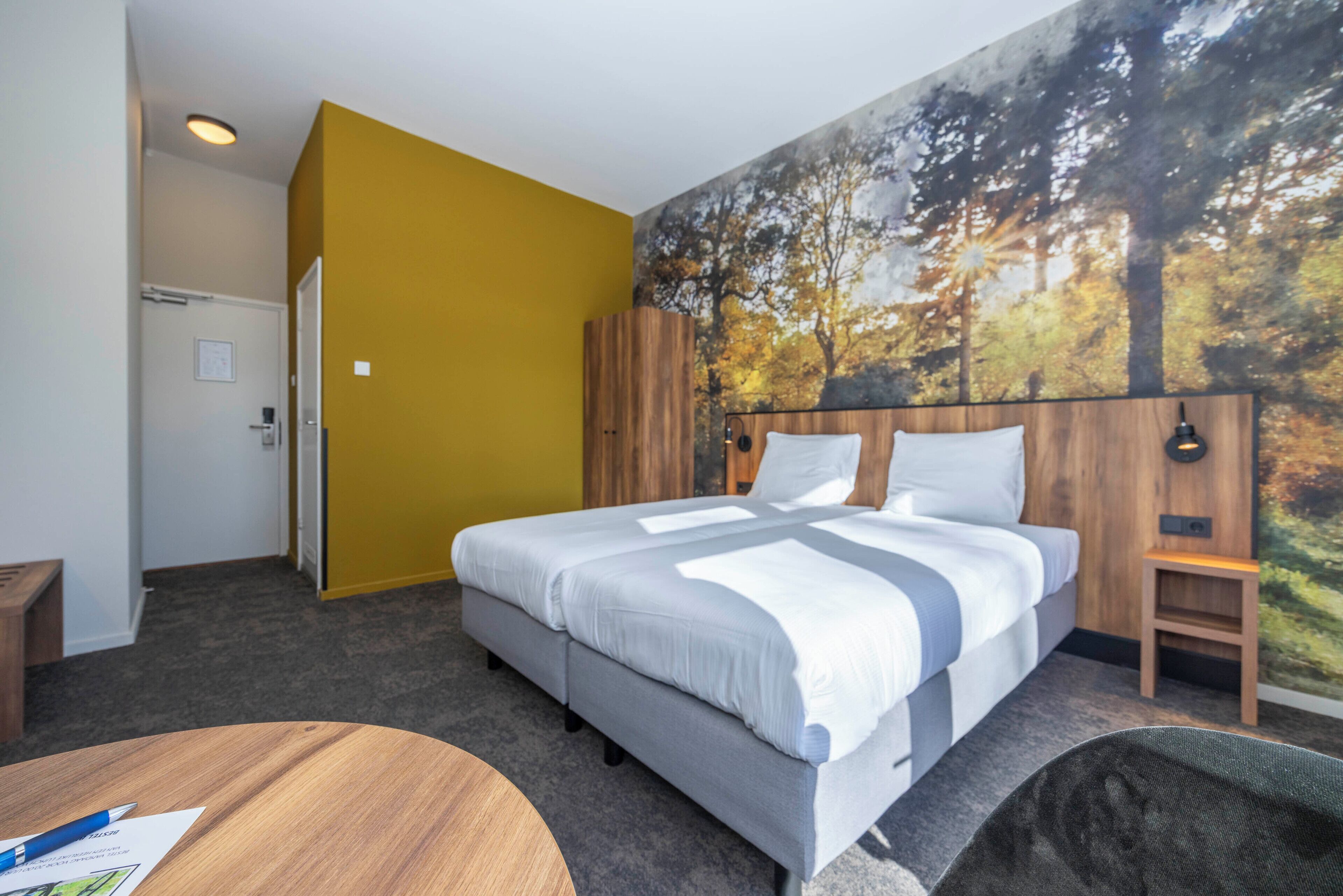 Une chambre d’hôtel avec un lit, une petite table, une chaise, une porte et une fresque murale.