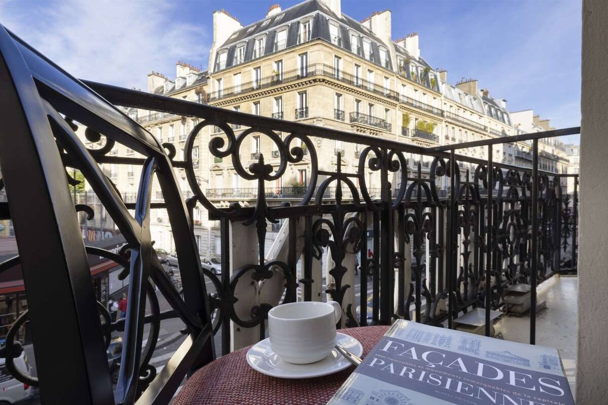 A balcony with wrought iron railings, a table with a white cup and saucer, and a book titled "FACADES PARISIENS".