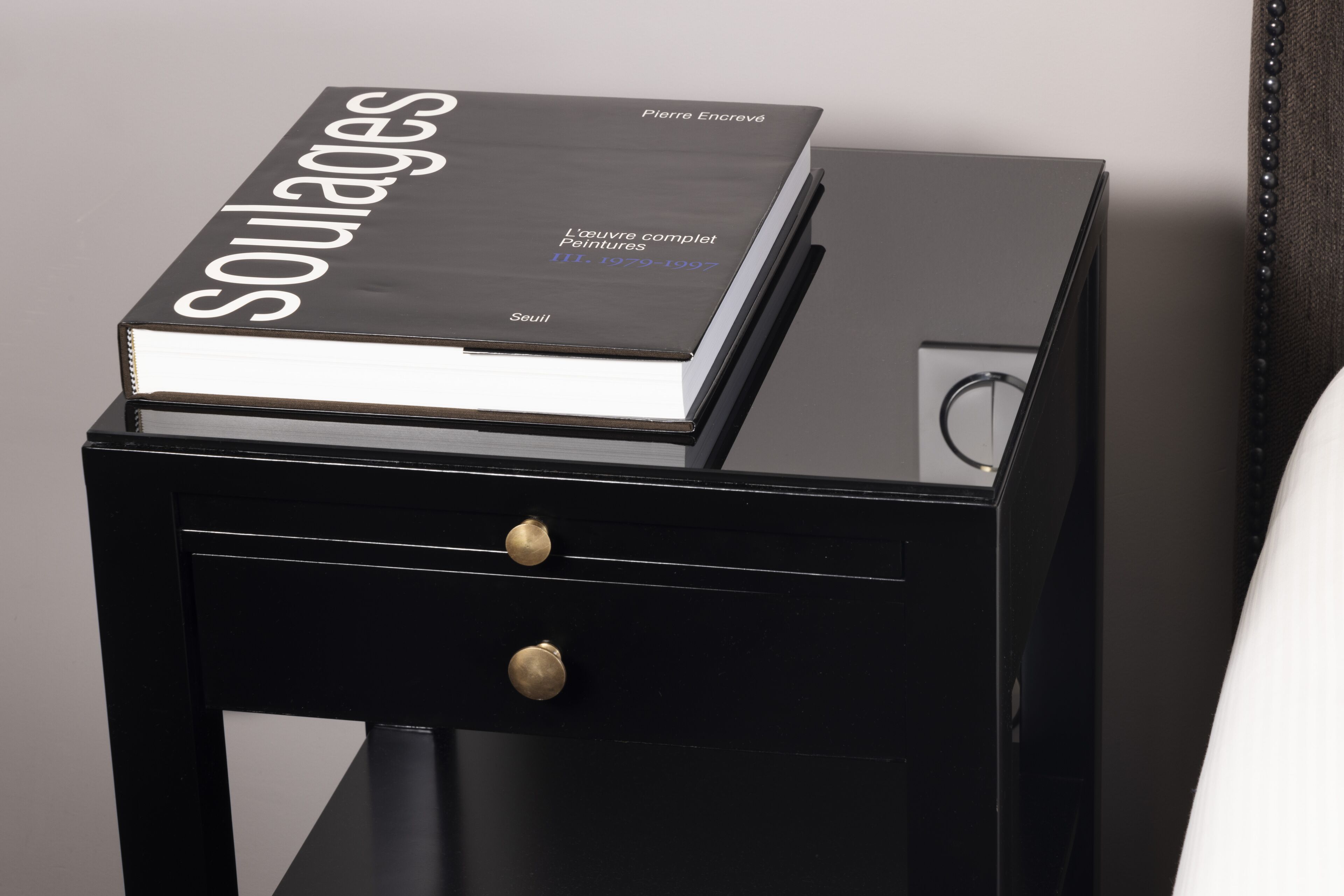 A black nightstand with a book titled 'Soulages' and a drawer with a knob.