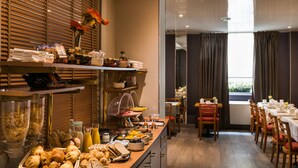 Un buffet de petit-déjeuner proposant une variété d’aliments et de boissons, un espace repas avec des tables et des chaises, et une vue sur l’extérieur grâce à de grandes fenêtres.