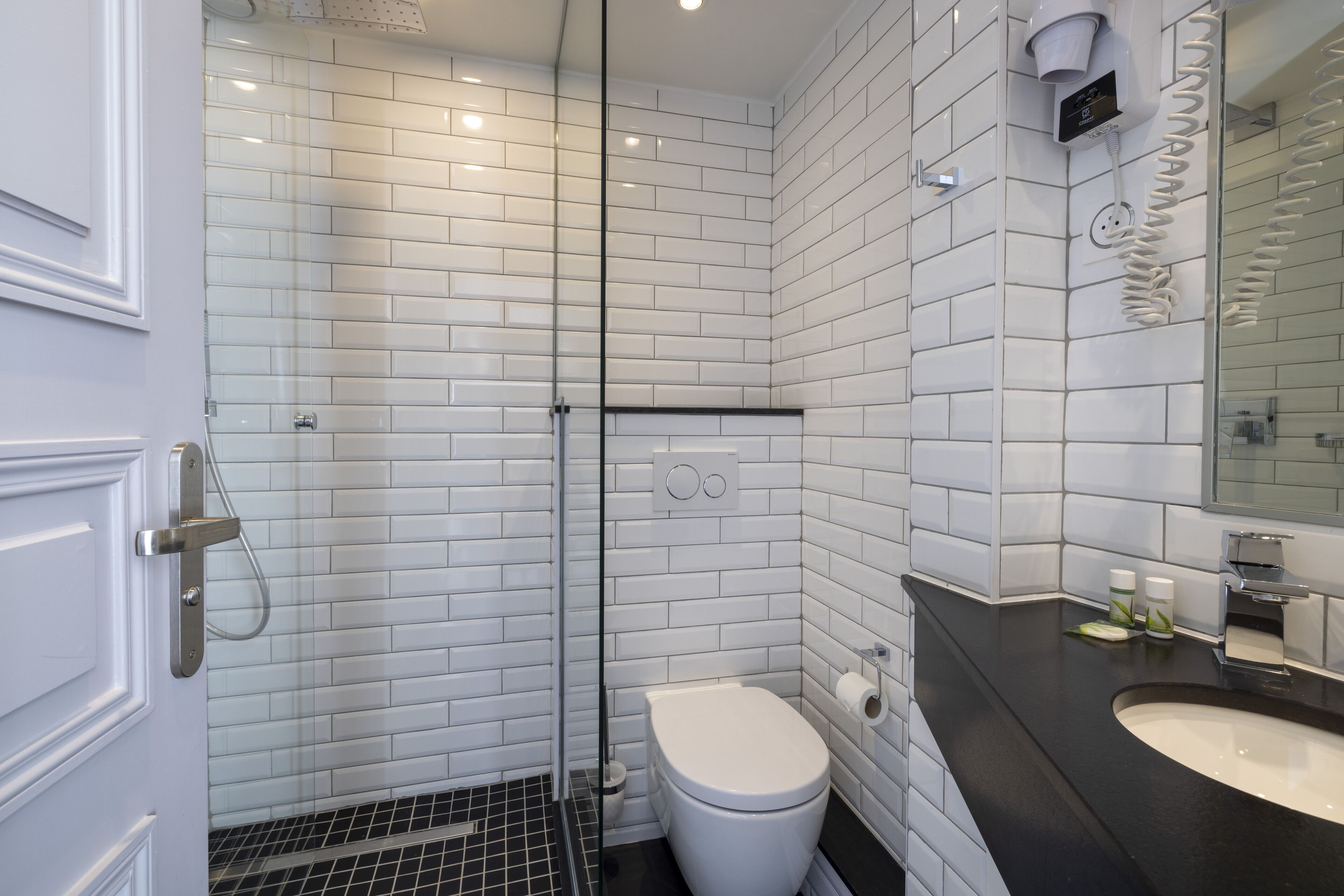 A modern bathroom with white subway tiles, a glass shower enclosure, a white toilet, and a black countertop with a sink and mirror.