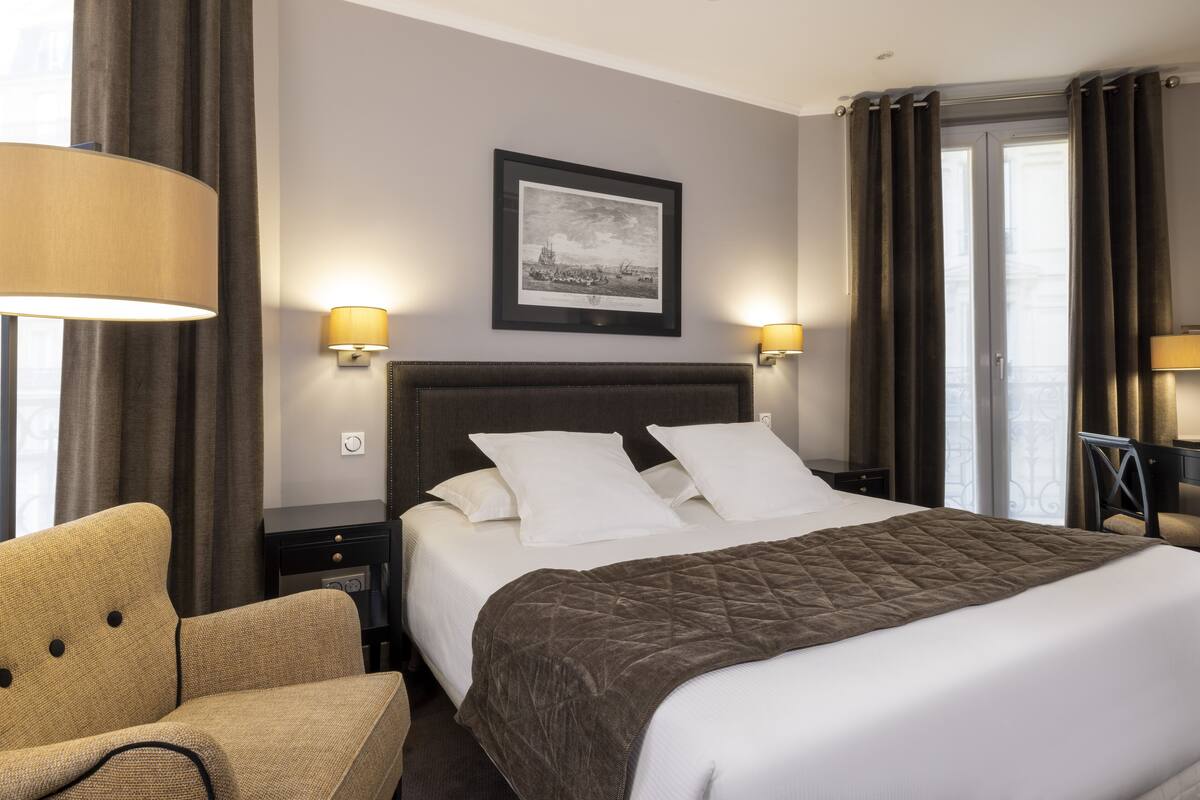 A hotel room with a large bed, two bedside lamps, a framed picture on the wall, and a chair.