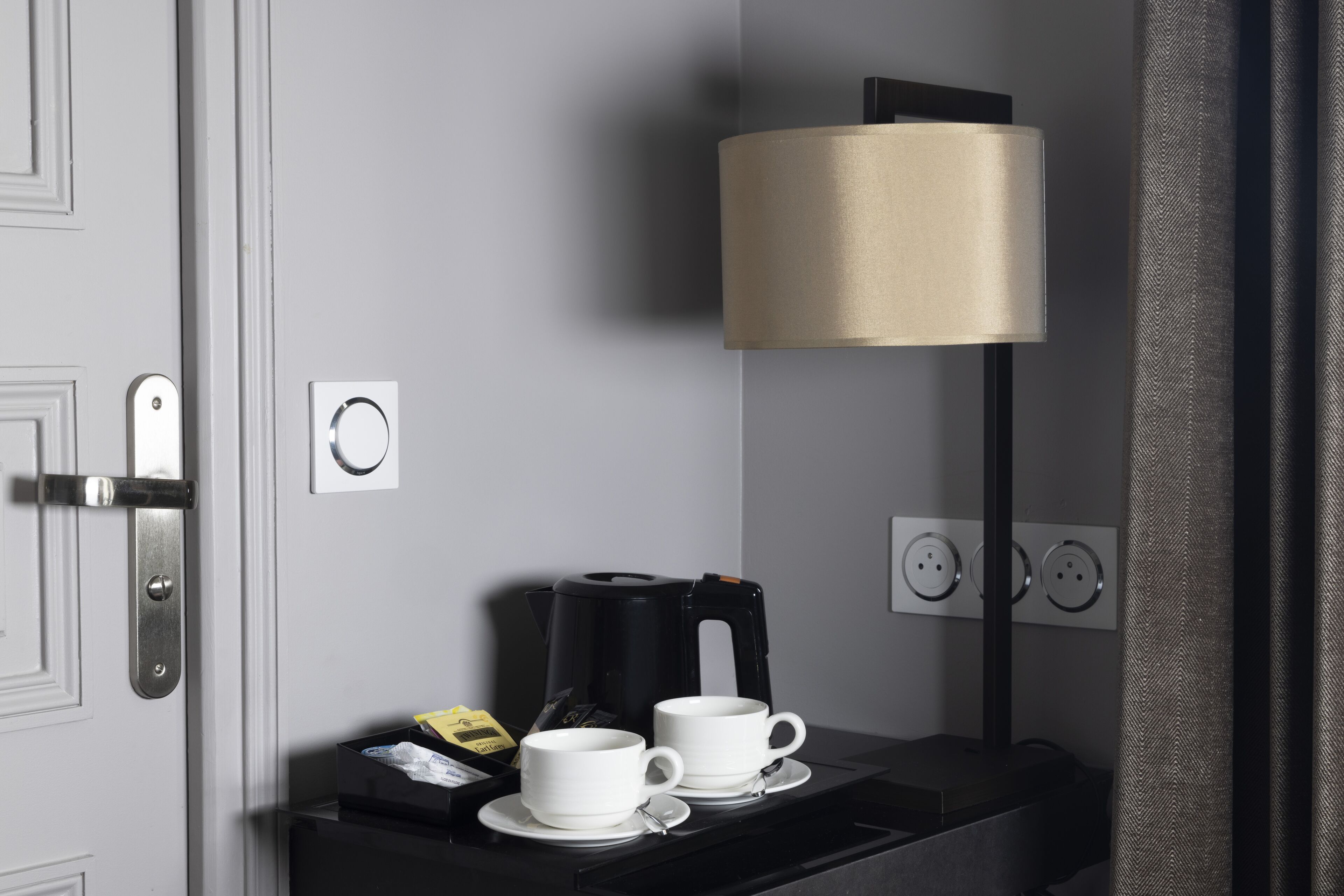 Habitación de hotel con una mesita negra que sostiene dos tazas blancas y una cafetera.