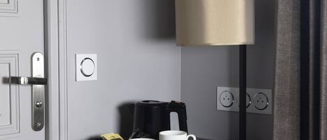 Habitación de hotel con una mesita negra que sostiene dos tazas blancas y una cafetera.