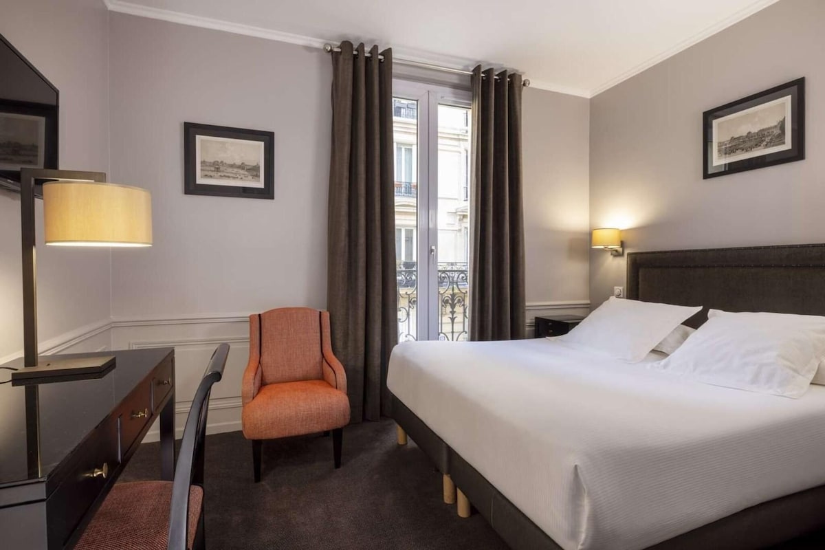 Une chambre d’hôtel avec un lit, une chaise, un bureau et une lampe.