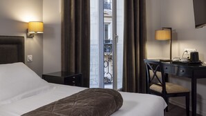 Une chambre d’hôtel avec un lit, un bureau, une chaise, une lampe et une vue sur le balcon extérieur.