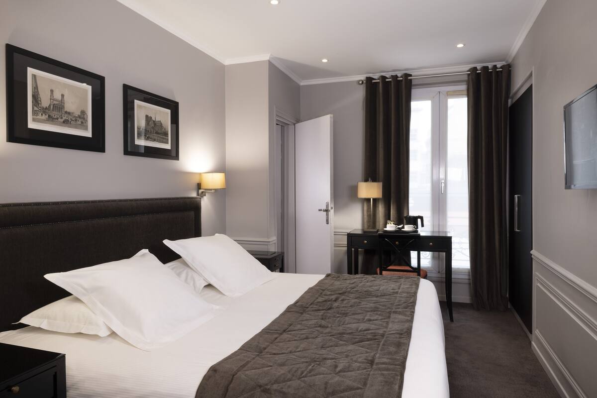 A hotel room with a large bed, a desk, and two framed pictures on the wall.