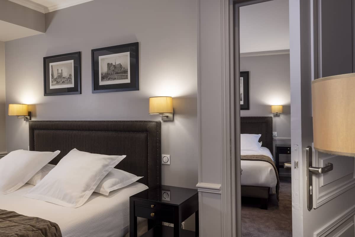 A hotel room with a bed, two bedside lamps, and two framed pictures on the wall.