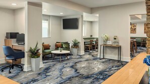 A modern hotel lobby with a marble floor, seating areas, a reception desk, and a TV mounted on the wall.